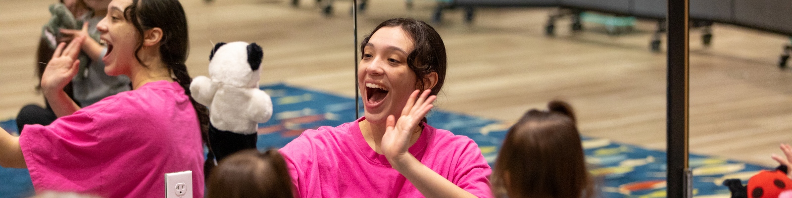 Image of a woman in pink shirt holding a panda puppet and waving