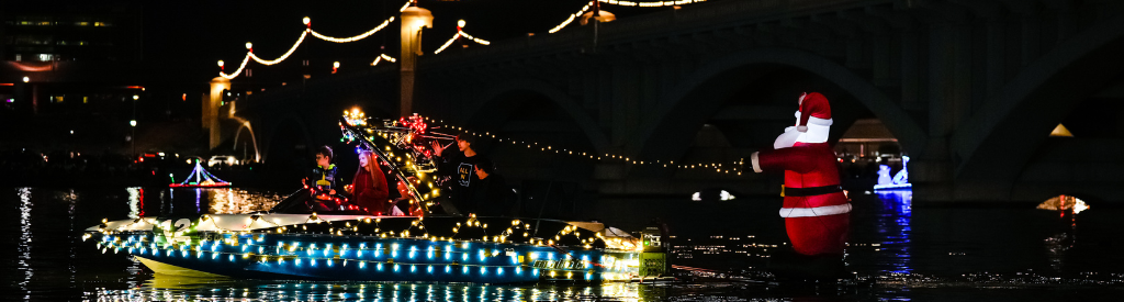 a speed boat covered in holiday lights pulls a blow-up Santa behind it at Tempe Town Lake during the boat parade