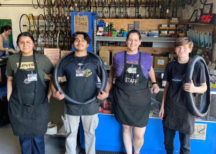 Three teens pose with staff member at internship site holding bike parks