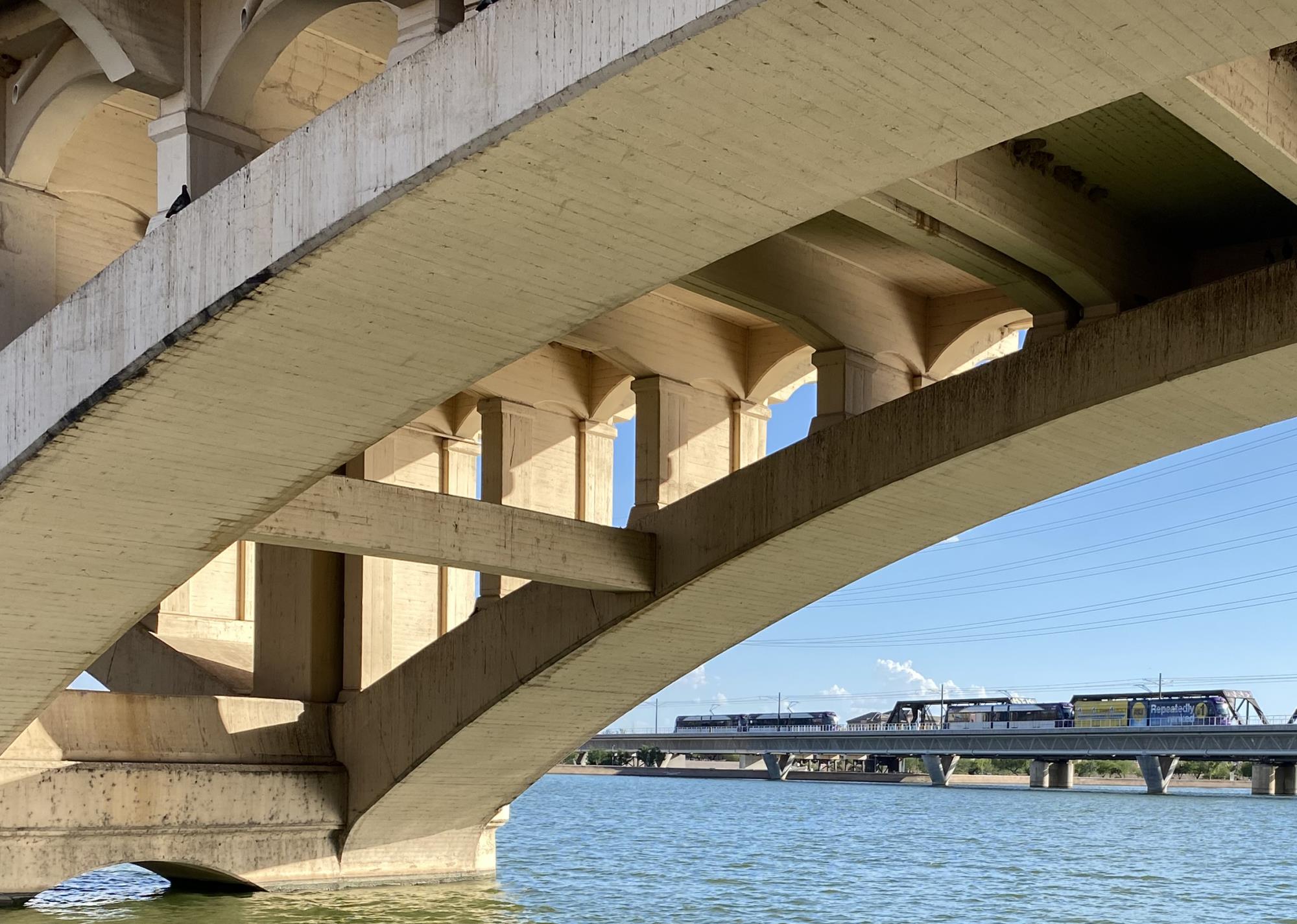 A photo take from Tempe Town Lake that showcases the Mill Avenue Bridge and the Light Rail bridge