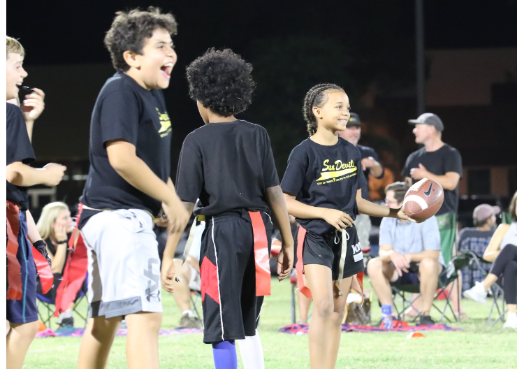 Photo of three youth playing flag football on the field in the evening