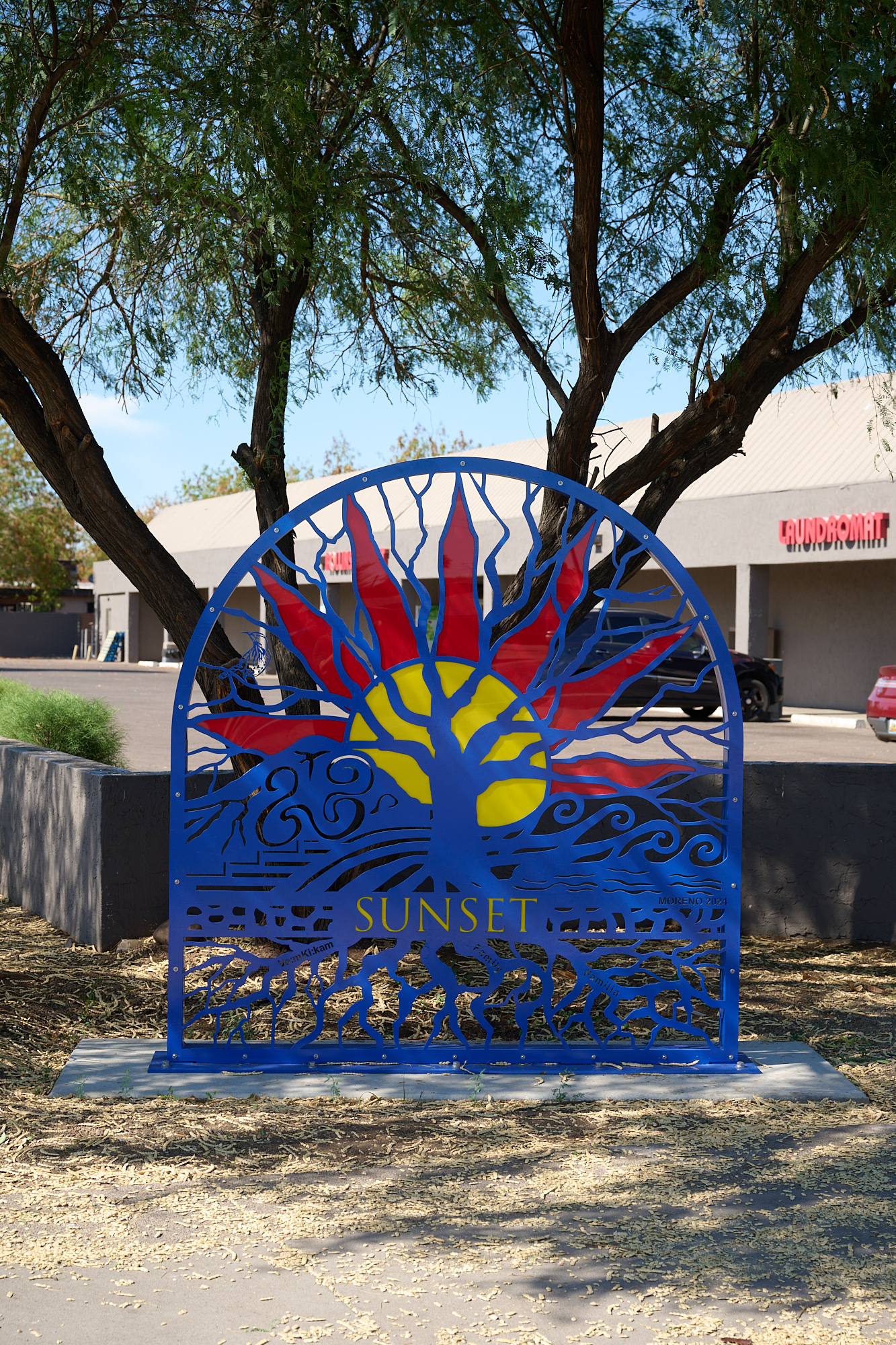 Steel sculpture depicting a tree of life against a sun and mountain. 