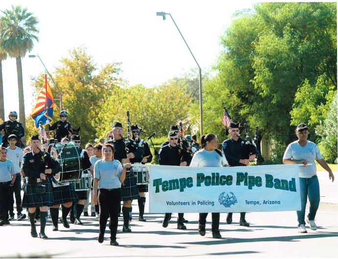 The Tempe Police Pipe Band marches together in front of their parade banner during a local parade.